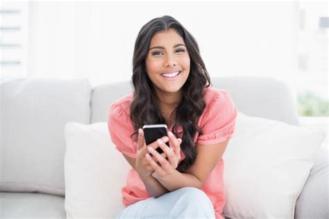 Premium Photo Cheerful Cute Brunette Sitting On Couch Holding Smartphone