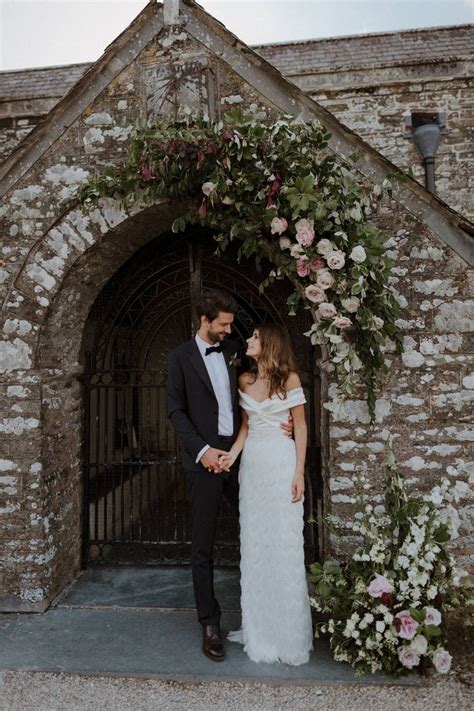 a bride and groom are standing in front of an archway with flowers on ...