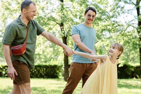 Familia gay feliz caminando junto con la hija adoptiva en el parque en día de verano Foto Premium