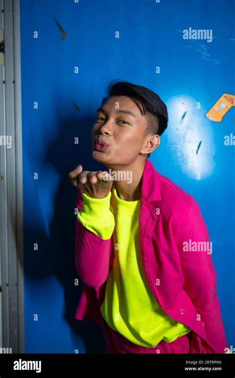 A Gay Asian Man Posing Very Funny And Humorous While Wearing A Pink Suit In Front Of A Blue
