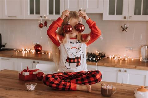 Una niña rubia con pijama rojo de navidad está sentada en la cocina y