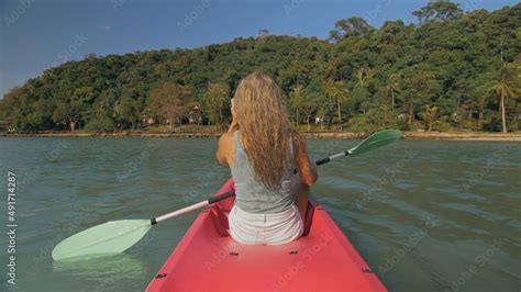 Long Haired Blonde Woman With Sunglasses Rows Bright Pink Canoe Along Sea Bay Water To Beach