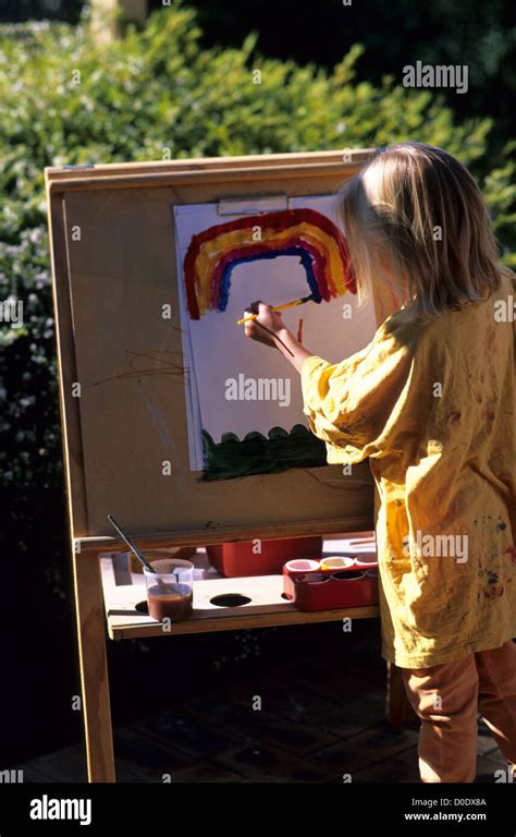 Child Painting A Rainbow On An Easel Outside In The Garden Stock Photo