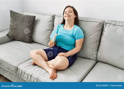 Brunette Frau Mit Daunensyndrom Sitzend Auf Dem Sofa Mit Handventilator Im Wohnzimmer Stockbild