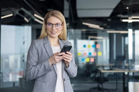 Blonde Businesswoman With Glasses Smiles While Holding Her Smartphone