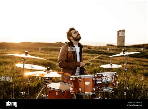A Guy Playing Drums In The Middle Of A Green Meadow On A Sunny Day