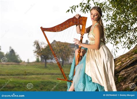 Portrait Naturel De Fille Blonde Du Caucase Dans La Jolie Robe Longue Jouant De La Harpe Sur La