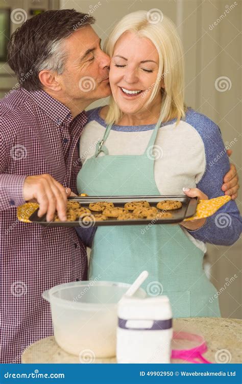 Mature Blonde Holding Fresh Cookies With Husband Kissing Her Stock Photo Image Of Domestic