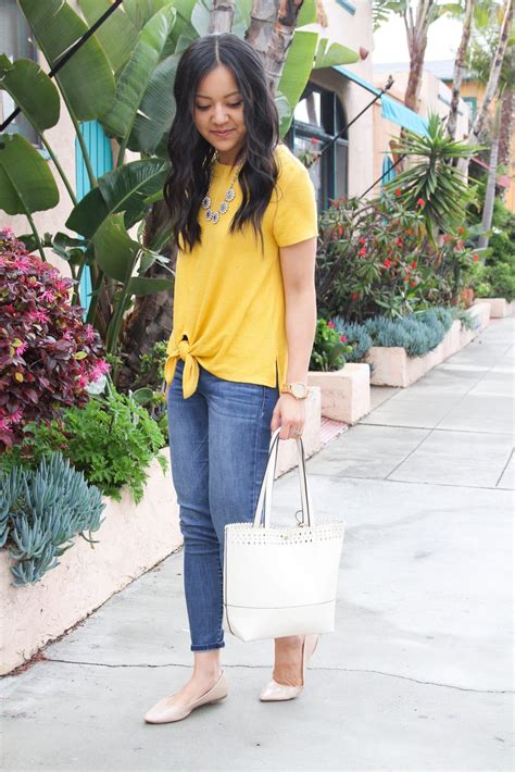Yellow Top Jeans Nude Flats Metallic Statement Necklace White Purse Looking Down Putting
