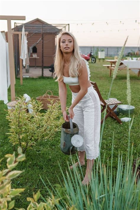 A Blonde Woman Is Watering Flowers In The Garden In The Courtyard Of A