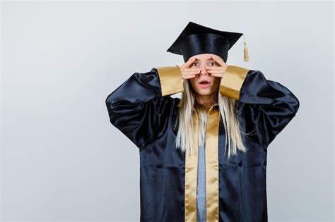 Fille Blonde En Robe De Graduation Et Casquette Montrant Des Signes V Sur Les Yeux Et à La