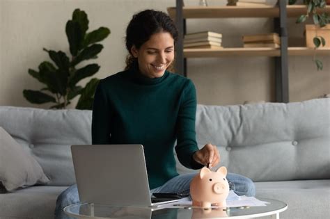 Ahorro de dinero Mujer latina casual feliz deja caer una moneda en la alcancía en el escritorio