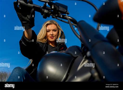 A Lovely Blonde Model Enjoys The Outdoor Weather While Posing With Her Motorcycle Stock Photo