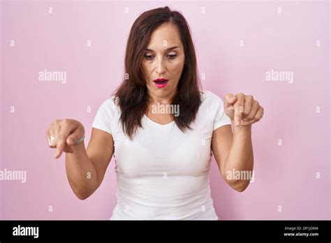 Middle Age Brunette Woman Standing Over Pink Background Pointing Down With Fingers Showing