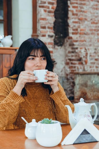 Imagen vertical de una joven latina sentada bebiendo té con precaución porque está muy caliente