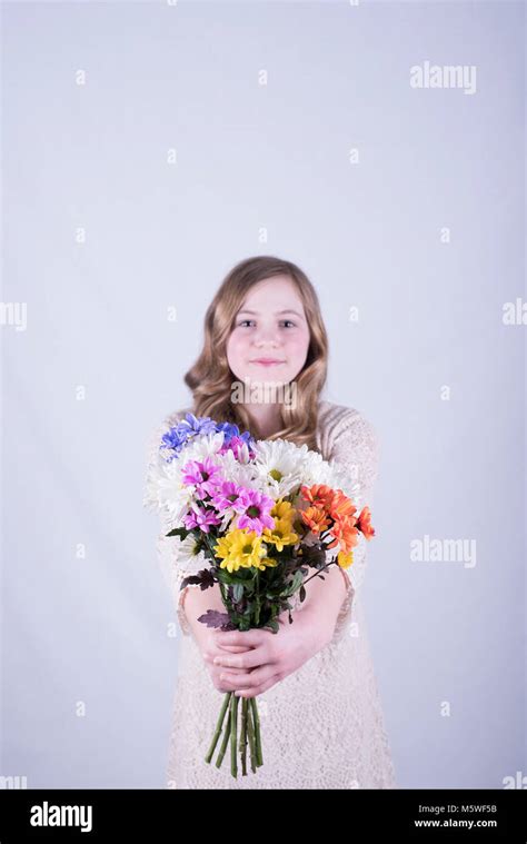 Smiling Twelve Year Old Girl With Long Dirty Blonde Hair Holding Out Colorful Bouquet Of