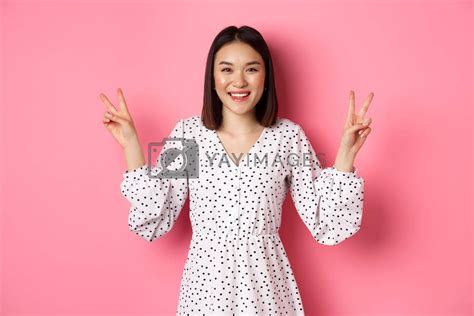 Cute Asian Brunette Girl In Dress Smiling Showing Kawaii Peace Signs And Looking Happy