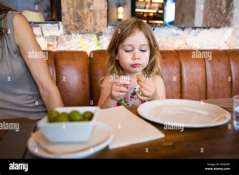 Four Years Age Blonde Girl Eating Next To Woman Mother Sitting In Brown Leather Sofa At
