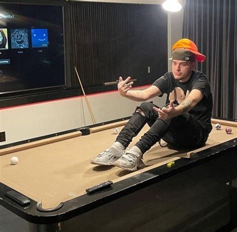 A Man Sitting On Top Of A Pool Table In Front Of A Flat Screen Tv