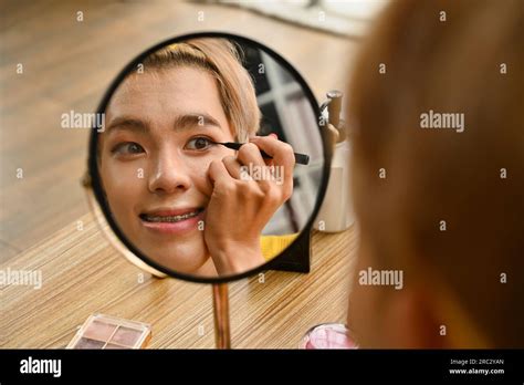 Beautiful Gay Man Looking At The Round Mirror And Applying Eyeliner LGBTQ Lifestyle And Makeup