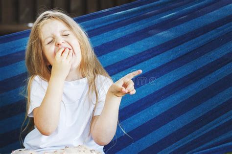 Petite Fille Blonde Aux Cheveux Longs Mange Une Fraise Dans Le Jardin Assis Dans Un Hamac Bleu