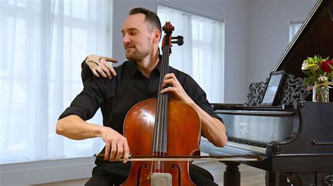 A Man Sitting In Front Of A Piano And Playing The Cello