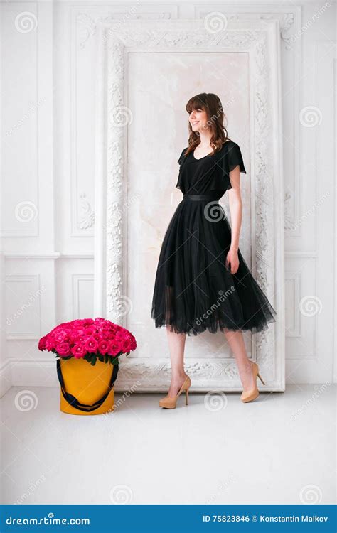 Gentille Jeune Fille Blonde Dans Une Robe Noire Et Des Chaussures Sur Des Talons Hauts Sentir