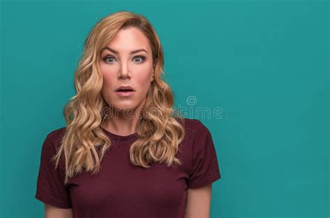 An Attractive Blonde On A Blue Background Is Surprised Or Shocked By Opening Her Eyes And Mouth