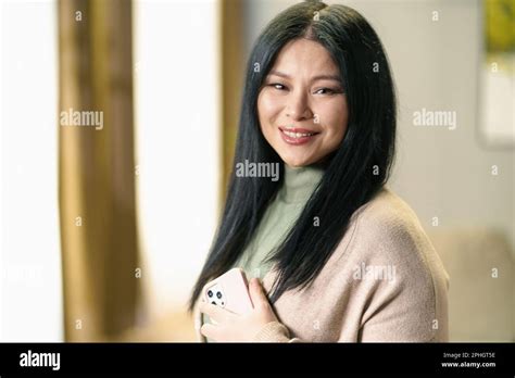 Mature And Positive Asian Woman With Thick Luscious Hair Holds Her Smartphone In Her Hand