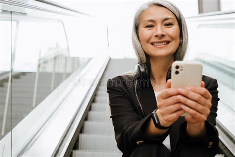 Mature Asian Woman Using Mobile Phone While Sitting On Escalator Stock Image Image Of