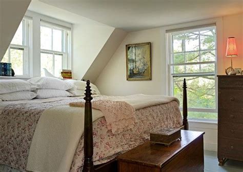 A Bed Sitting Under Two Windows Next To A Dresser And Window Sill In A