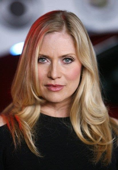A Woman With Blonde Hair And Blue Eyes Looks At The Camera While Standing In Front Of A Red Car