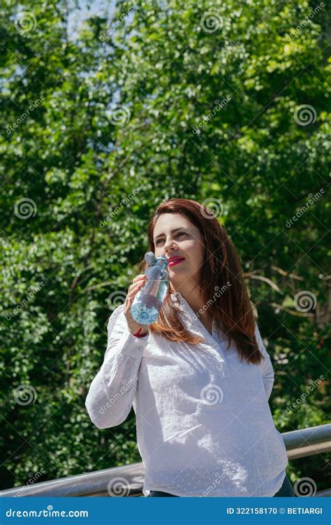 Mature 45 Year Old Woman With Long Hair And Red Lips Drinking Water From A Bottle In Nature On A