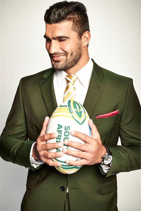 A Man In A Green Suit Holding A Rugby Ball And Smiling At The Camera