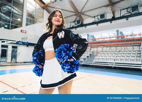 Medium Shot Of Brunette Short Haired Cheerleader In A Jacket Posing With Blue Shiny Pom Poms In