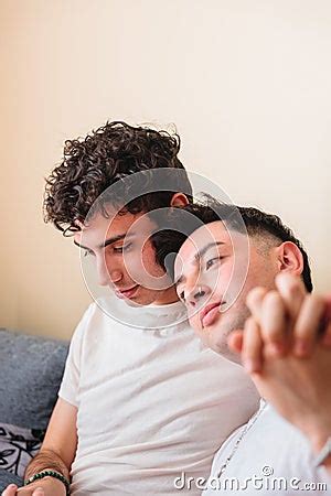 Snuggling Latin Gay Couple In Pajama On The Sofa Taking Hands And Sharing A Relaxing Moment Out