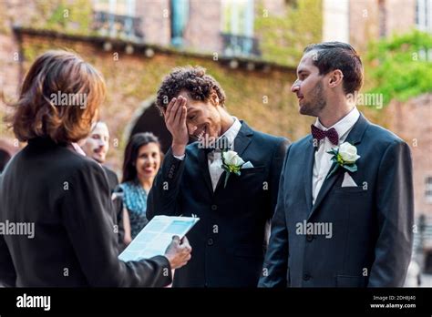 Gay Man Looking At Shy Partner While Standing In Front Of Priest During Wedding Ceremony Stock