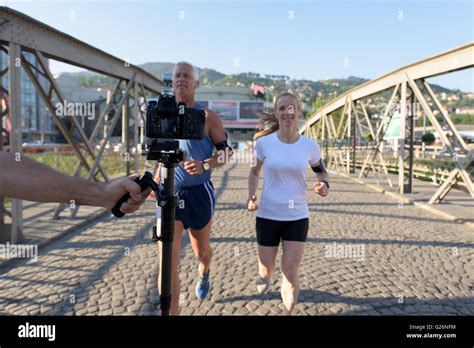 Healthy Mature Couple Jogging In The City At Early Morning With Sunrise In Background Stock