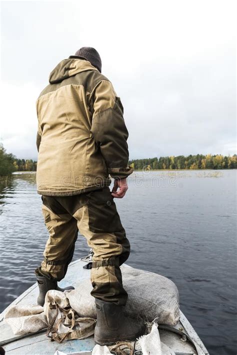 A Fisherman In Camouflage Stands At The Bow Of The Boat And Collects