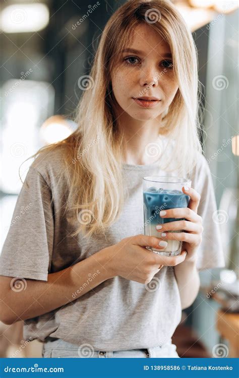 A Good Looking Slim Blonde Girl Wearing Casual Style Sits On The Chair And Holds A Cup Of