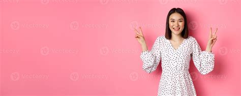 Cute Asian Brunette Girl In Dress Smiling Showing Kawaii Peace Signs And Looking Happy