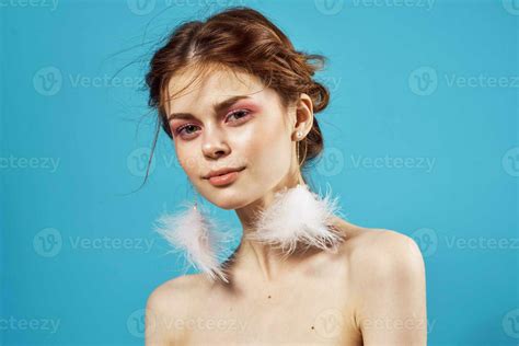 Woman With Bright Makeup On Naked Shoulders And Fluffy Earrings Fashion Blue Background Close Up