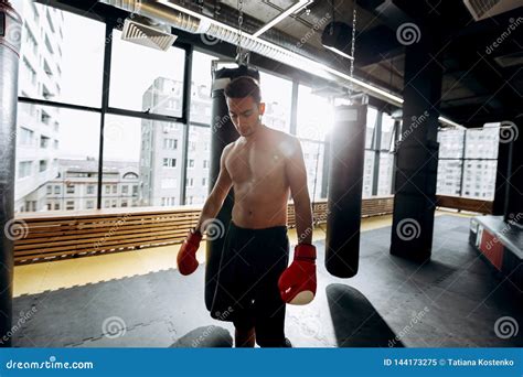 Sportsman In Red Boxing Gloves With A Naked Torso Dressed In The Black Shorts Stands Next To The