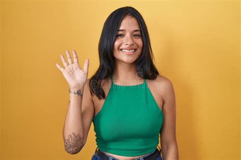 Brunette Woman Standing Over Yellow Background Waiving Saying Hello Happy And Smiling Friendly