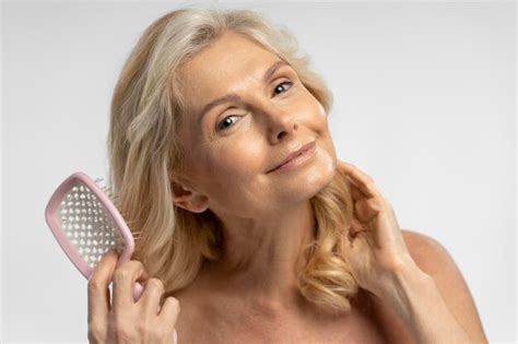 Premium Photo Mature Blonde Woman Combing Hair With Hairbrush Smiling At Camera Isolated On