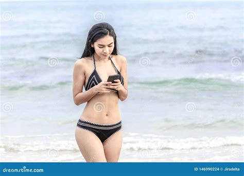 Mujer Tailandesa En Bikini Negro Que Camina En La Playa Y Que Juega Con Su Smartphone Foto De