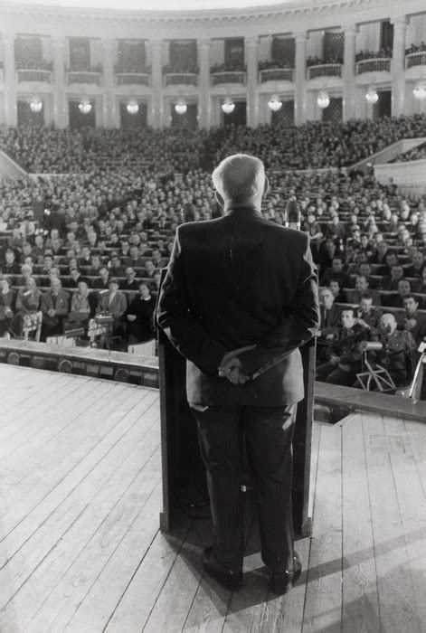 Man Standing On Stage And Addressing A Large Room Of People