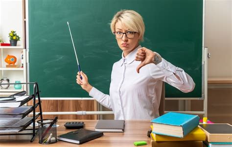 Jeune Enseignante Blonde M Contente Portant Des Lunettes Assise Au Bureau Avec Des Fournitures