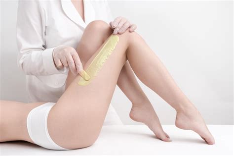 Premium Photo Cosmetologist Applying Green Hot Wax On Slim Woman Leg Using Spatula While Woman