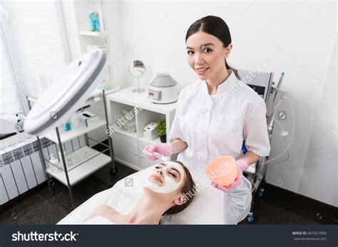 Positive professional cosmetologist is holding brush and bowl ...
